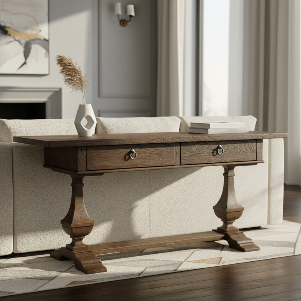 Dark wood console table with two drawers, carved bulbous pedestals, and trestle base behind beige sofa in bright room