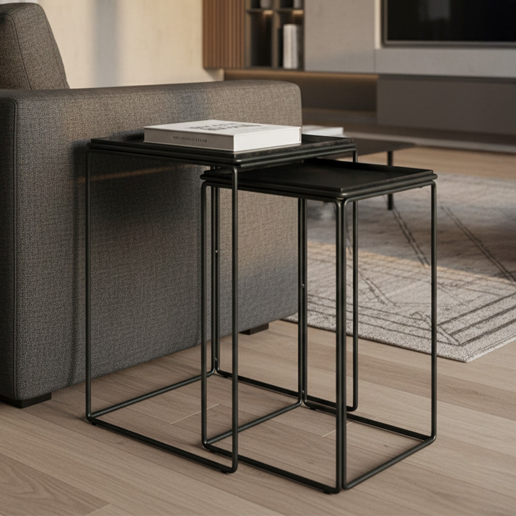 Set of two nesting tables with dark nickel glazed iron and steel tray tops and slim metal frames by sofa in living room